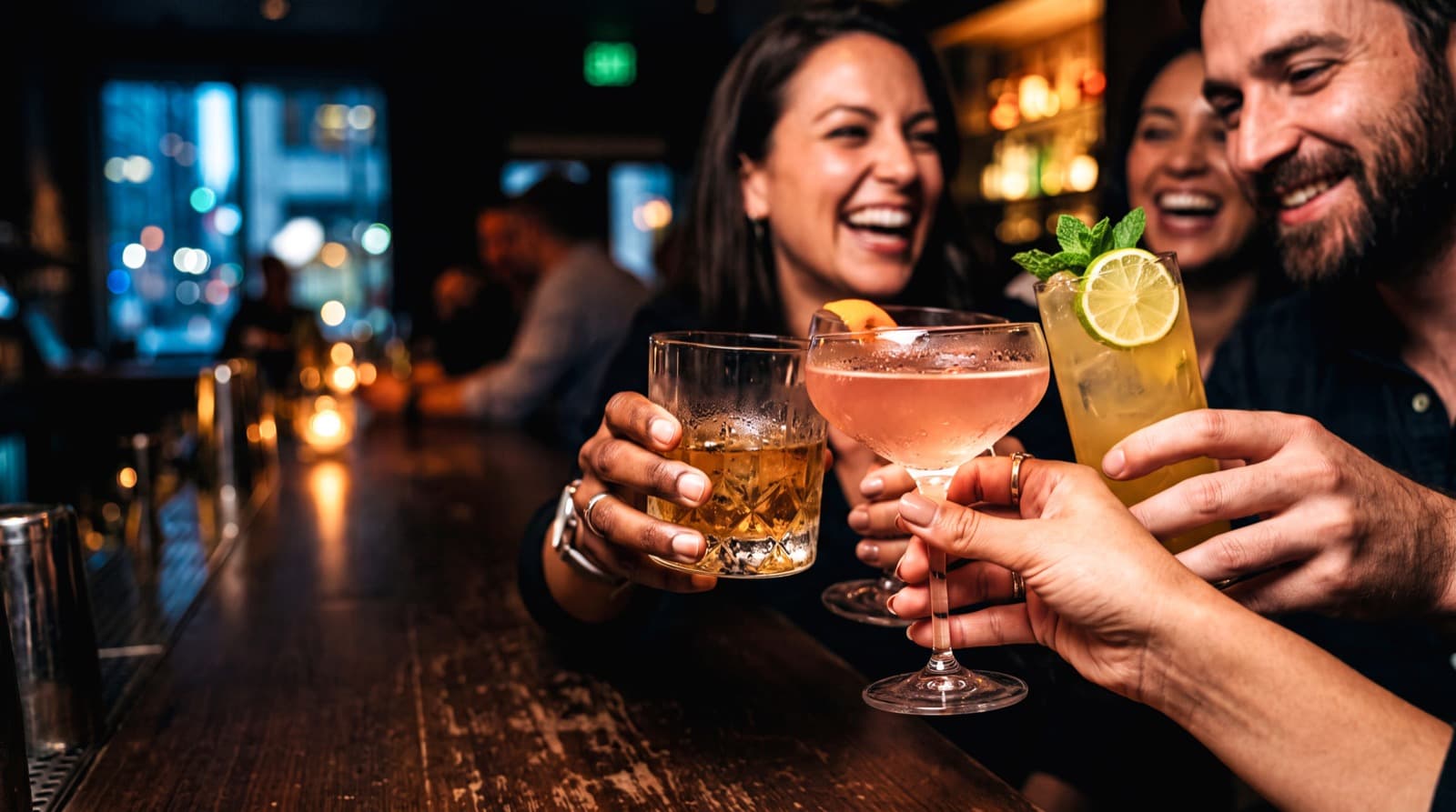 Three people raising cocktails together at a bar